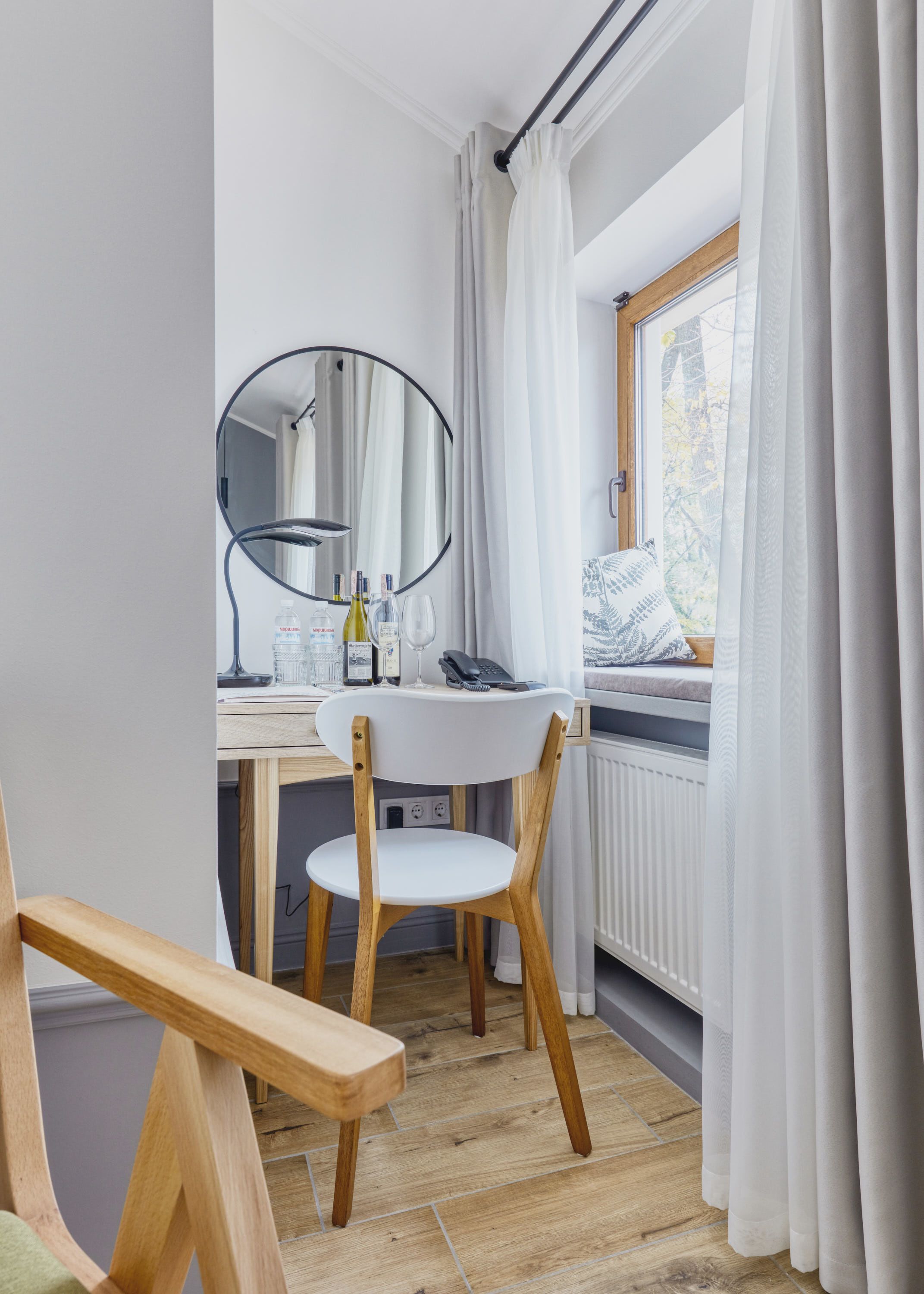A compact bedroom with a wooden desk, a chair, a mirror, and a window with curtains.
