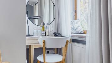 A compact bedroom with a wooden desk, a chair, a mirror, and a window with curtains.