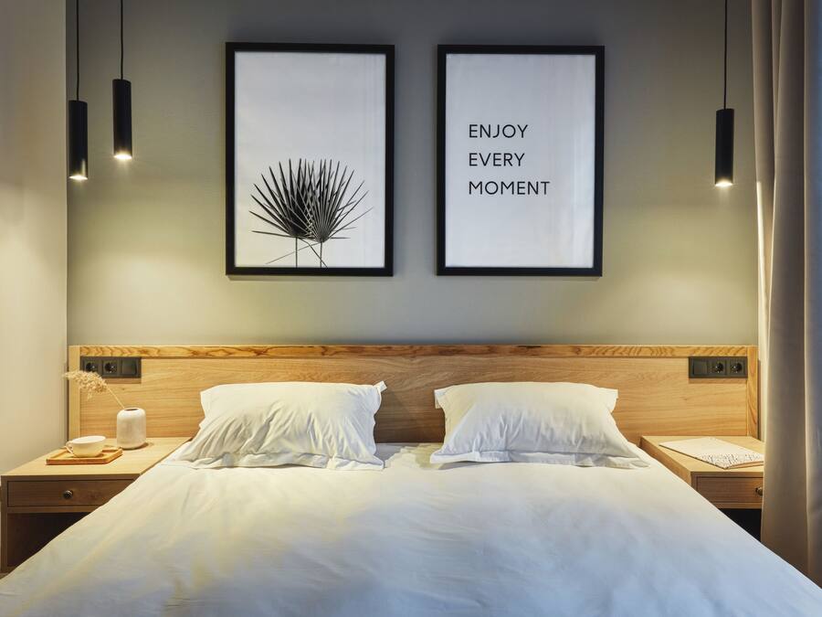 Un lit double bien fait, avec du linge de lit blanc, deux tables de chevet avec des lampes et deux tableaux encadrés accrochés au mur.