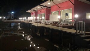 A waterfront hotel with a red exterior, a covered deck with seating, and a reflection in the water. - Bua Villa (Pathio)
