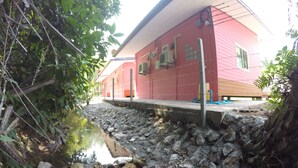 A red building with a stone retaining wall and a small stream. - Bua Villa (Pathio)