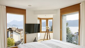 A hotel room with two beds, a large window with a view of mountains and a lake, a tripod with a camera, and a flat-screen TV mounted on the wall. - Hotel Rössli Gourmet & Spa (Weggis)