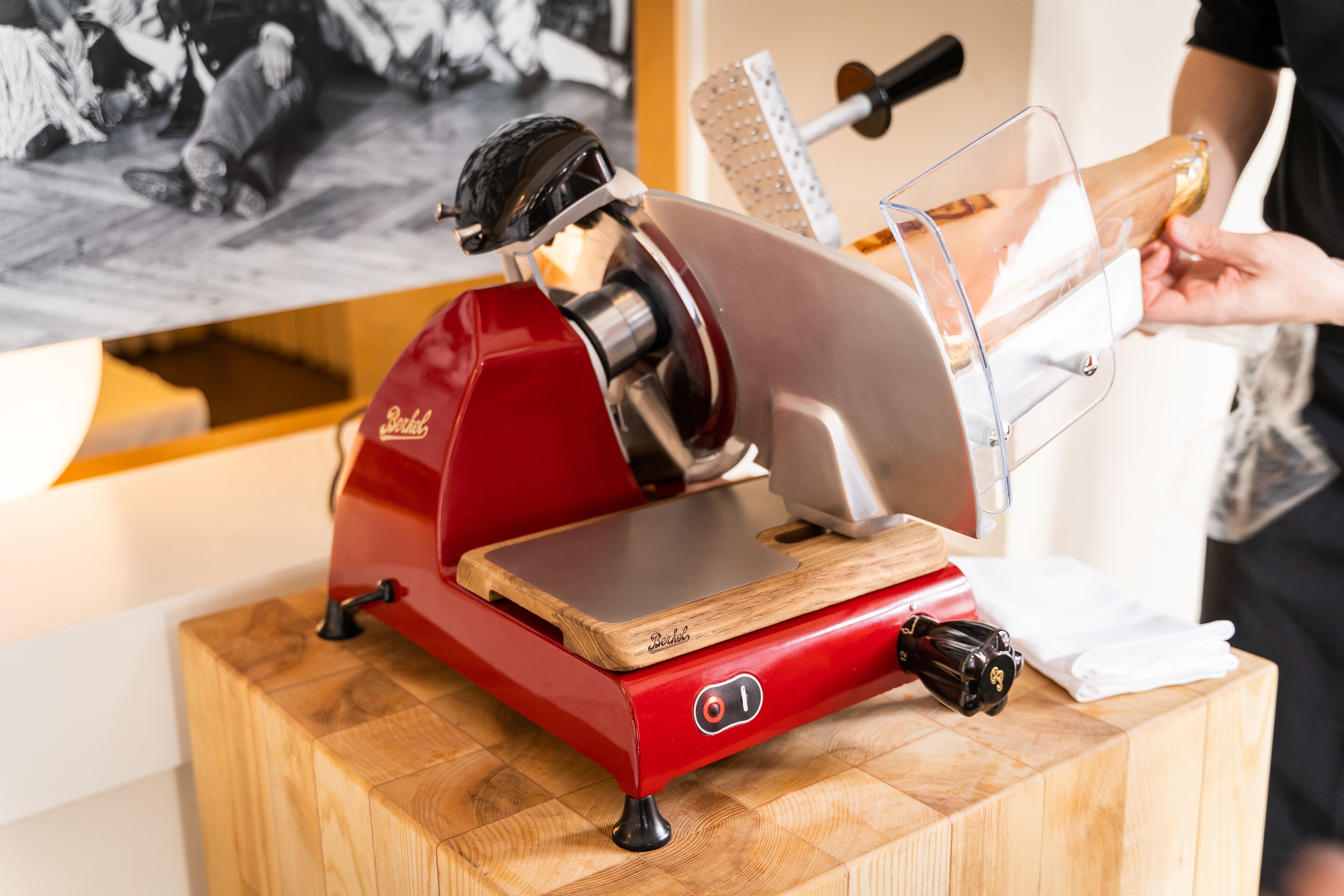 A red meat slicer on a wooden block with a person using it.
