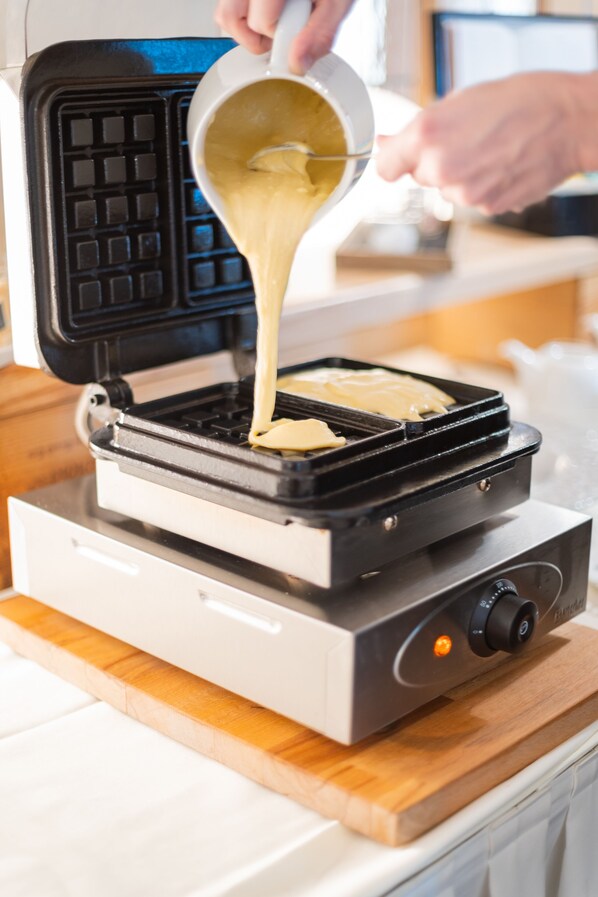 A waffle iron on a kitchen counter with batter being poured into it. - Hotel Rössli Gourmet & Spa (Weggis)
