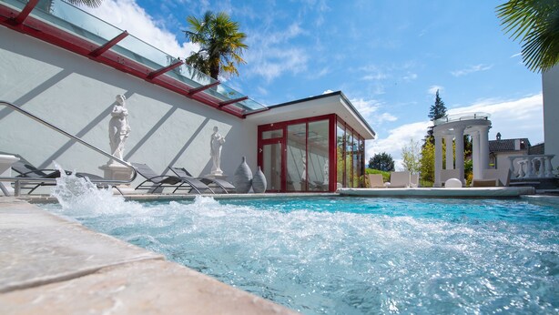 A swimming pool with a glass-enclosed area, statues, and a palm tree. - Hotel Rössli Gourmet & Spa (Weggis)