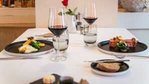 A dining table with plates of food, wine glasses, and a vase with a rose. - Hotel Rössli Gourmet & Spa (Weggis)