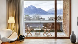 A room with a sliding glass door leading to a balcony with a view of mountains and a lake. There is a chair, a small table with a vase, and a fan on the balcony floor. - Hotel Rössli Gourmet & Spa (Weggis)