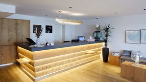 A modern reception desk with a wooden finish, a computer, and a potted plant. - Hotel Rössli Gourmet & Spa (Weggis)