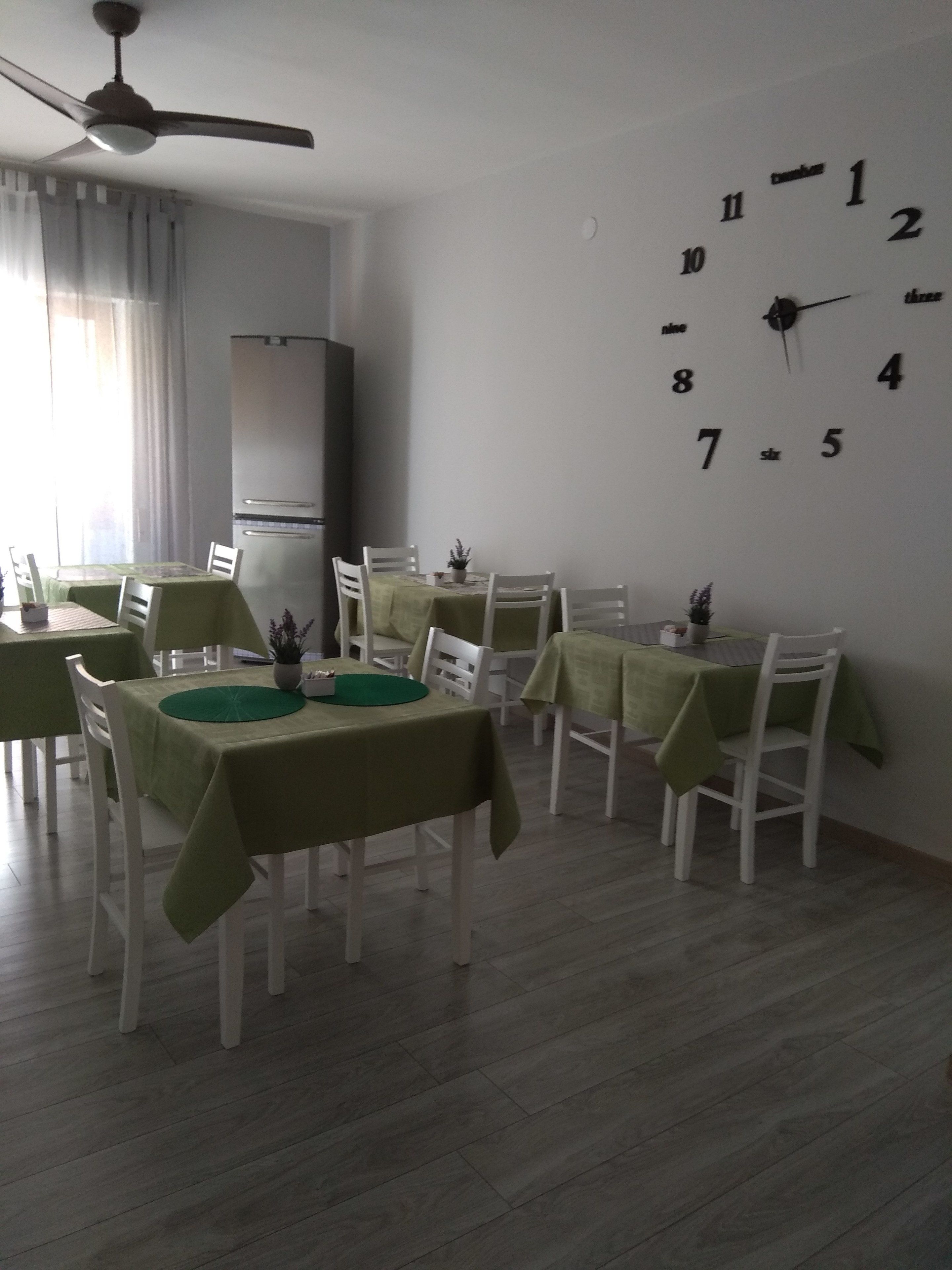 A dining area with tables and chairs, a clock on the wall, and a ceiling fan.