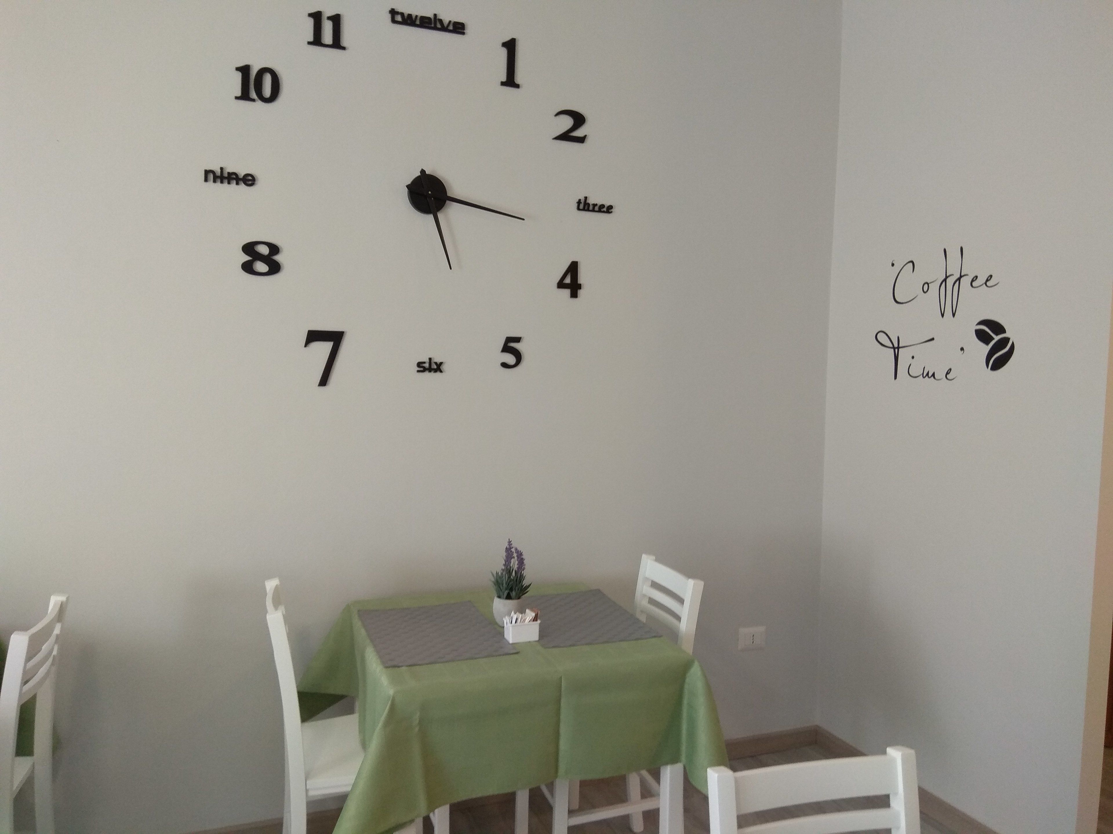 Una habitación con una mesa verde y sillas blancas, un reloj de pared y un letrero que dice 'Coffee Time'.
