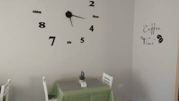Una habitación con una mesa verde y sillas blancas, un reloj de pared y un letrero que dice 'Coffee Time'.