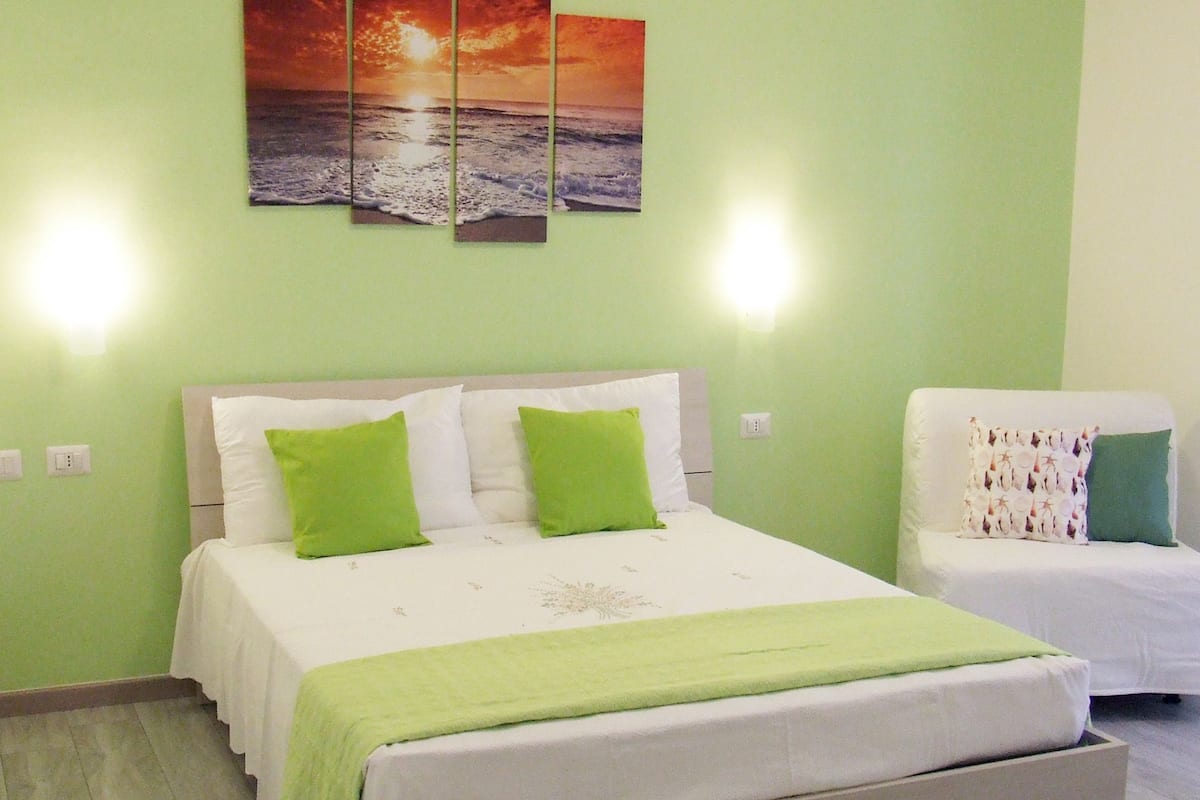 A room with a bed, a chair, and a wall-mounted picture.