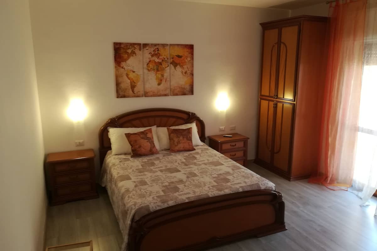 A bedroom with a wooden bed, two bedside tables, a wardrobe, and a world map artwork on the wall.