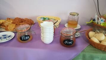 Una mesa con alimentos, incluyendo frascos etiquetados “Perro” y “Fichi”, una cesta de pan y una taza de té.