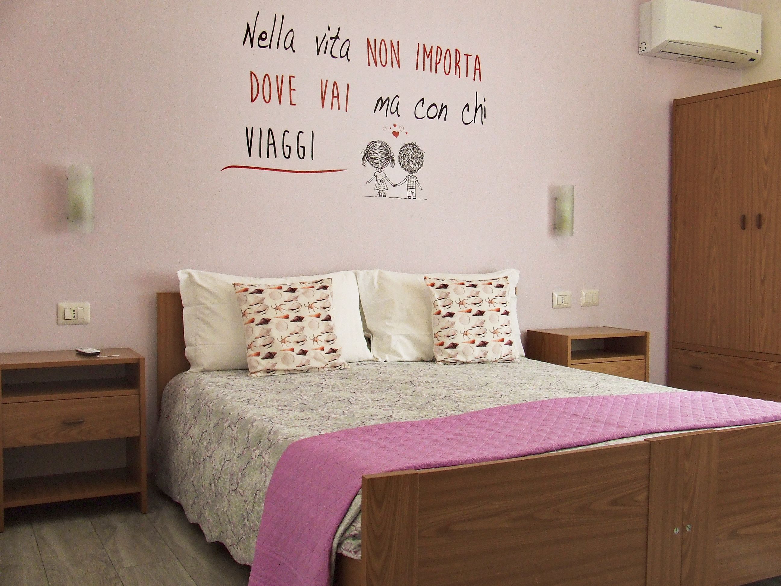 A bedroom with a bed, two bedside tables, a wardrobe, and a wall with a motivational quote.