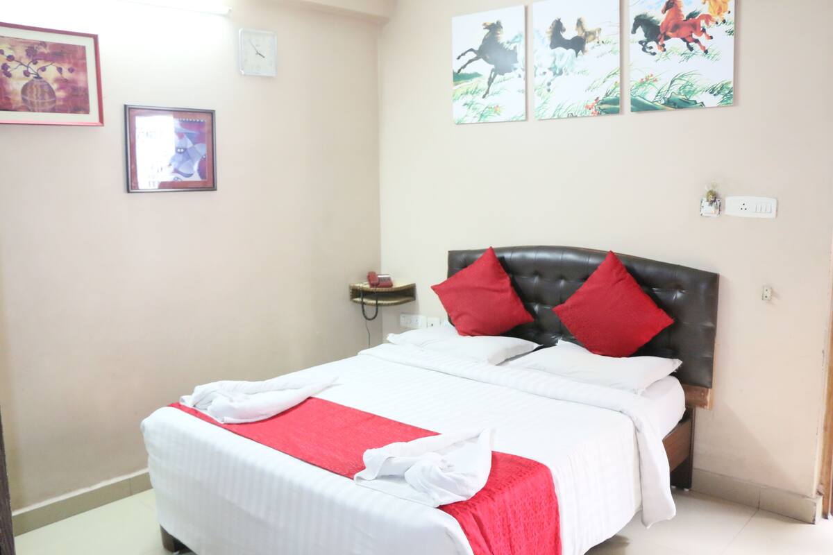 A neatly made bed with red and white bedding, a black headboard, and a small bedside table with a lamp.