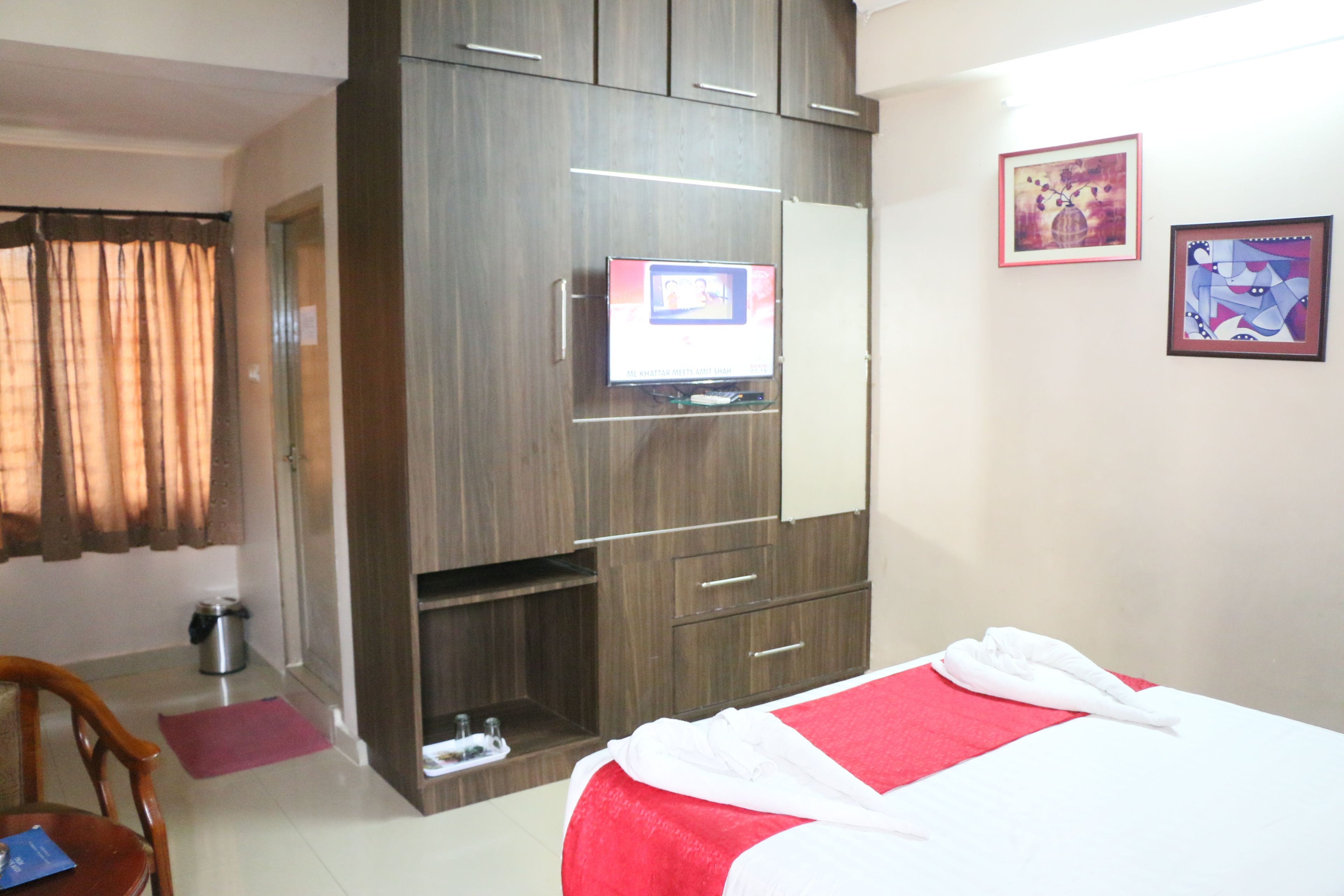 A hotel room with a bed, a TV mounted on a wooden cabinet, a trash bin, and a door.
