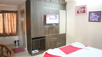 A hotel room with a bed, a TV mounted on a wooden cabinet, a trash bin, and a door.