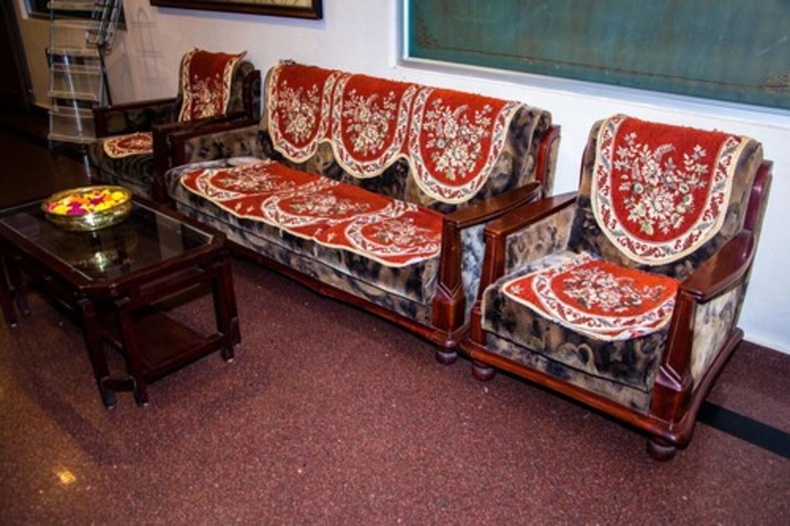 A traditional sofa set with ornate red and white covers, a wooden coffee table with a decorative bowl, and a window with a view.