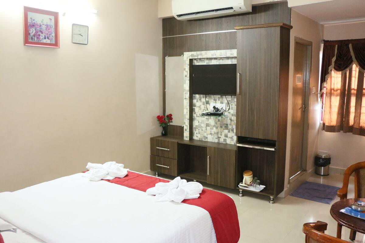 A hotel room with a bed, a wardrobe, a mirror, a small table with a vase of flowers, and a window with curtains.