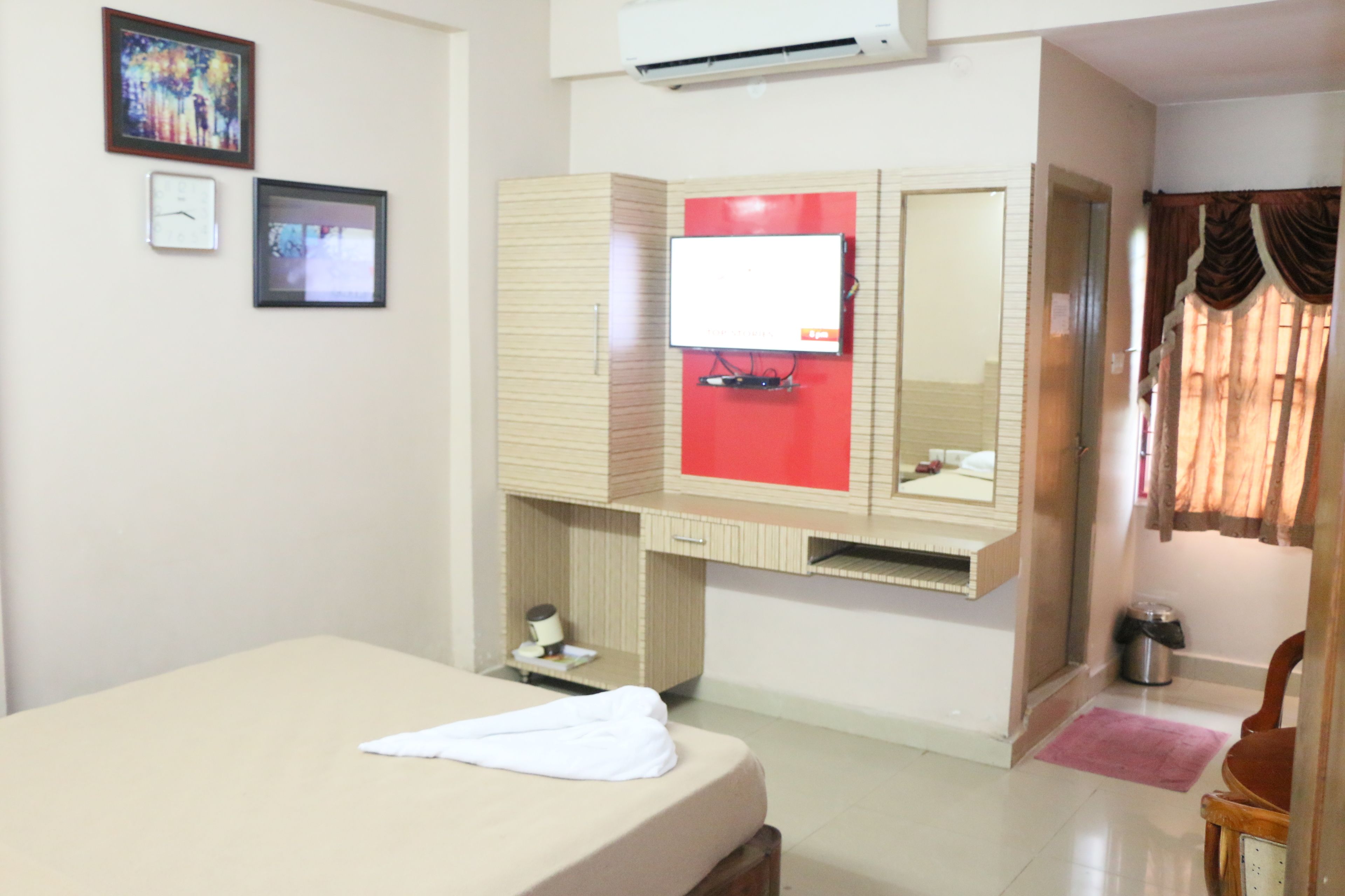 A hotel room with a bed, a mirror, a TV, and a window with curtains.
