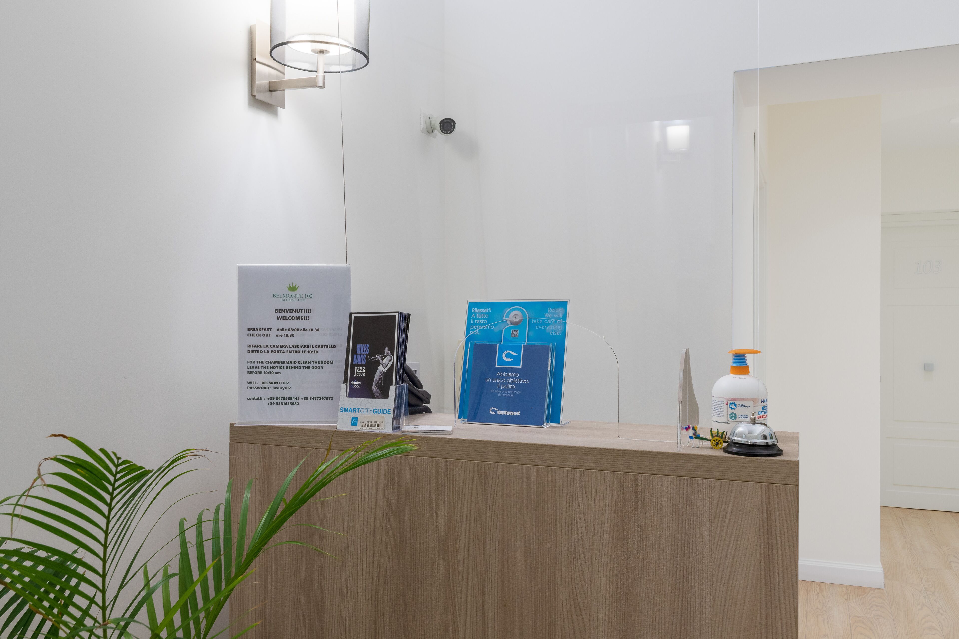 Una recepción con carteles informativos, una planta y un dispensador de desinfectante de manos.