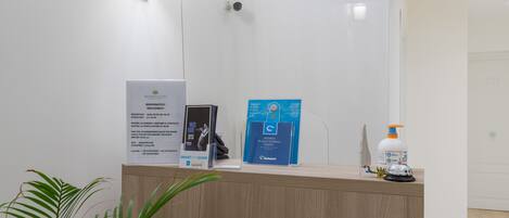 Una recepción con carteles informativos, una planta y un dispensador de desinfectante de manos.