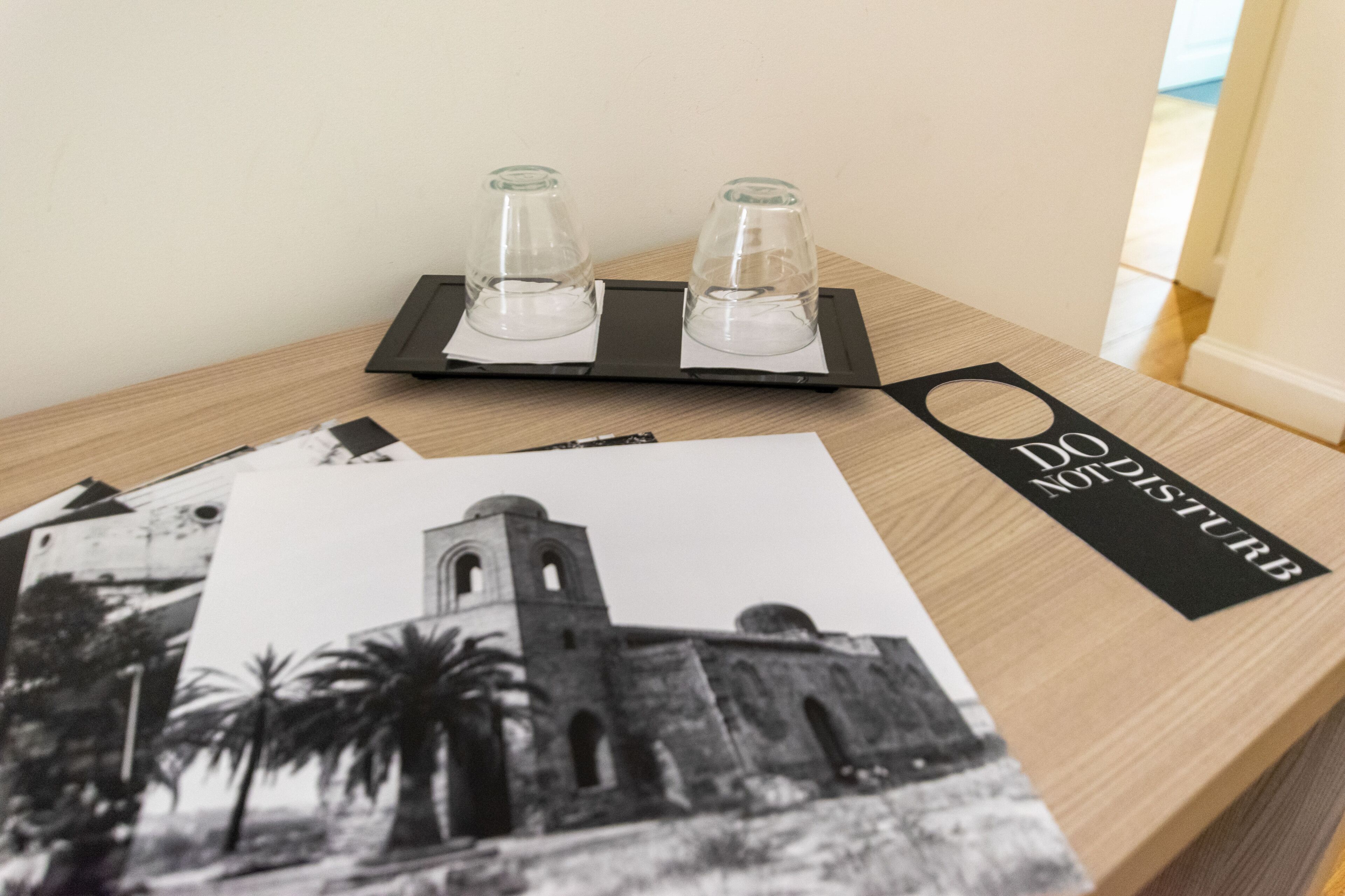 Una mesa de madera con una bandeja negra que sostiene dos vasos transparentes, una fotografía blanco y negro de un edificio, y un letrero negro con texto blanco.