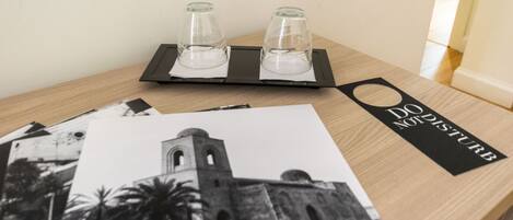 Una mesa de madera con una bandeja negra que sostiene dos vasos transparentes, una fotografía blanco y negro de un edificio, y un letrero negro con texto blanco.