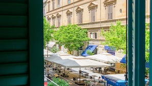 Vista de una calle con mesas al aire libre, un edificio de arquitectura clásica y un marco de puerta verde.