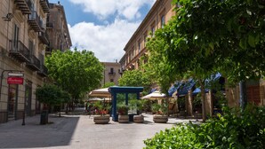 Una plaza empedrada con un quiosco azul, rodeada de edificios con balcones y terrazas.