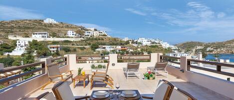 An outdoor terrace with a view of a hillside town, wooden furniture, and a table set for dining.