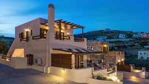 A modern two-story house with a stone facade, wooden accents, and a pergola. - Syra Suites (Syros)