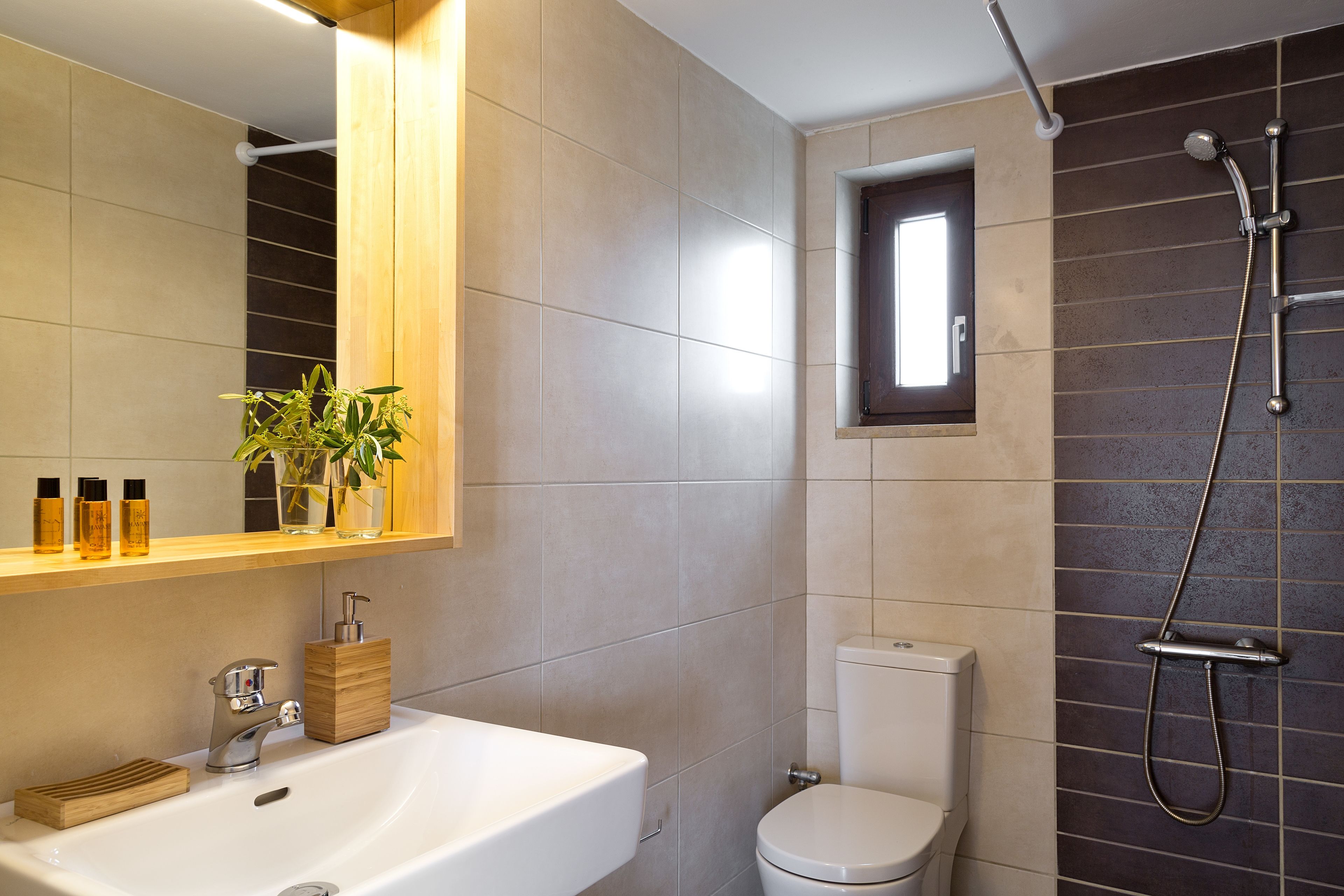 Ein modernes Badezimmer mit einem weißen Waschbecken, einem hölzernen Seifenspender und einem kleinen Fenster über der Toilette.