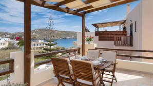 A terrace with wooden furniture, a table set for dining, and a view of the sea and hills. - Syra Suites (Syros)