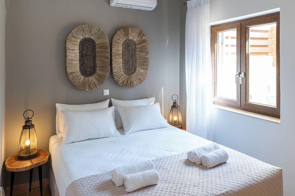 A neatly made bed with white linens and towels, a bedside table with a lantern, and two wall-mounted decorative items.