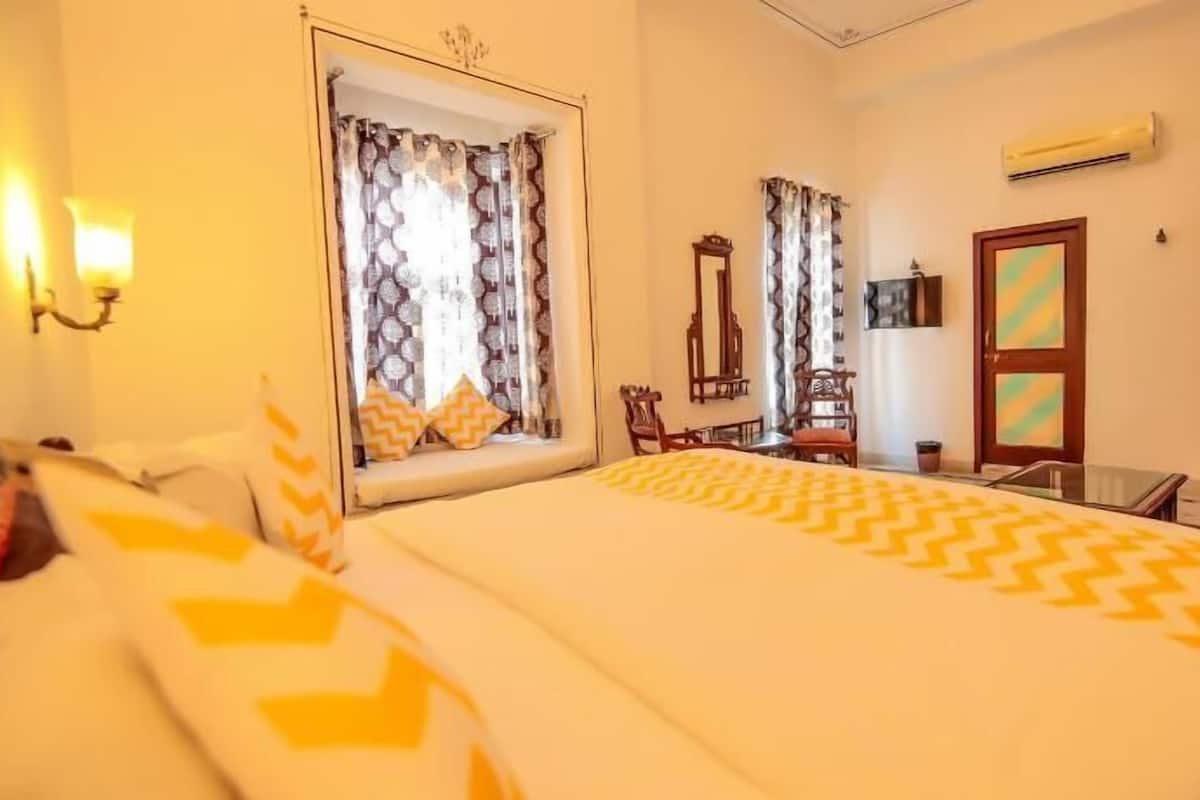 A hotel room with a large bed, a desk, a chair, a mirror, and an air conditioning unit.