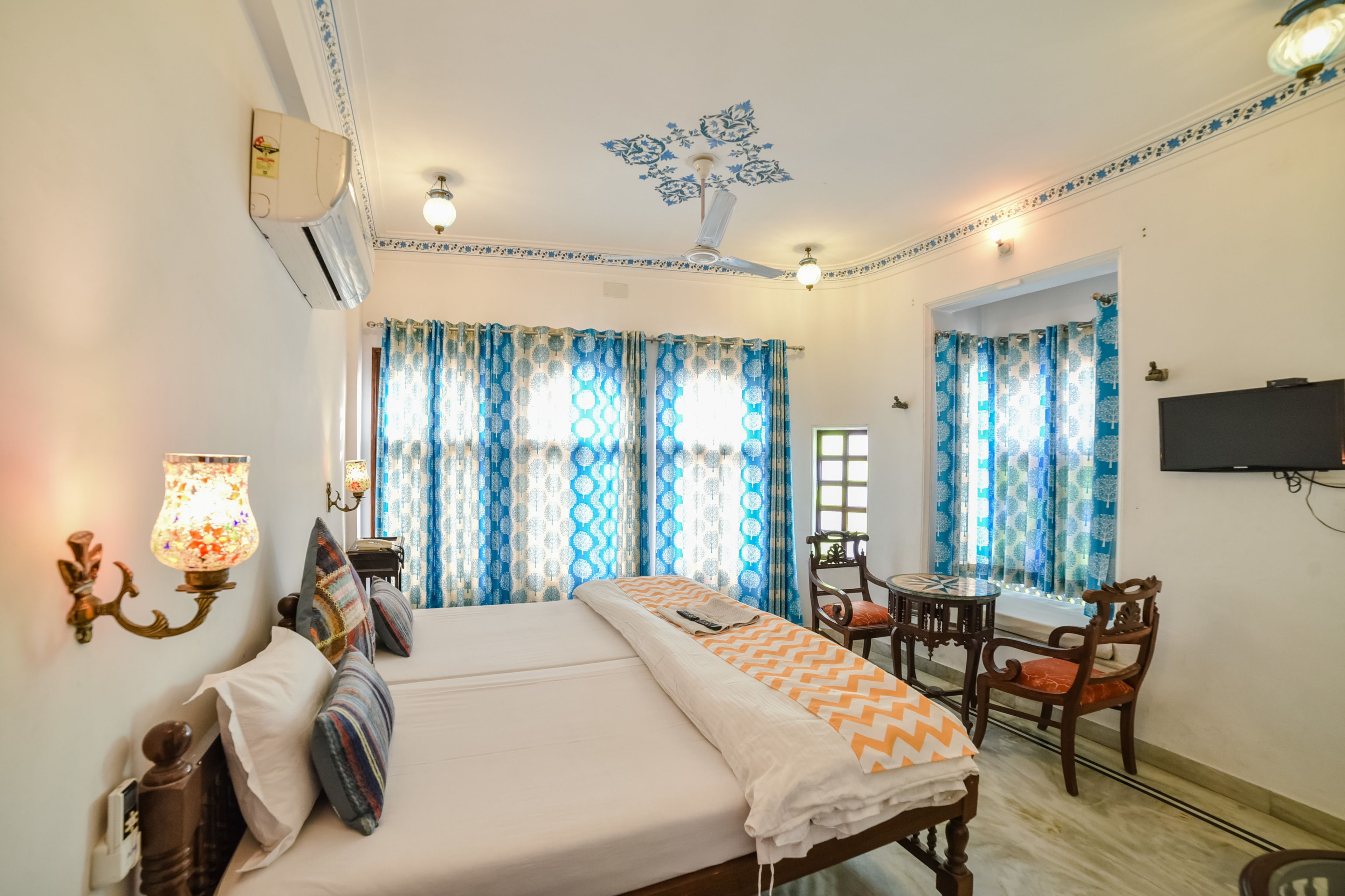 A hotel room with a bed, a desk, a chair, a TV, and a window with curtains.