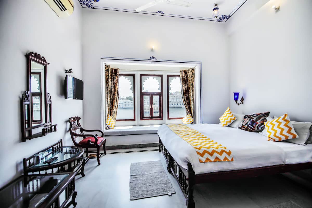 A bedroom with a bed, a desk, a chair, a window with curtains, and a view of the outside.