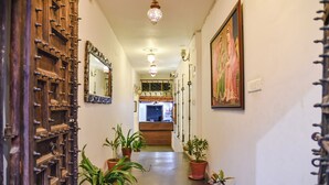 Un pasillo con plantas en macetas, una puerta de madera con tachuelas de metal y un cuadro en la pared.