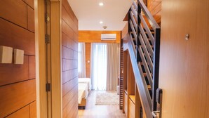 A hallway with wooden paneling, a staircase, and a bed in the distance.