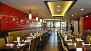 A spacious restaurant with long tables, booths, and a red textured wall.