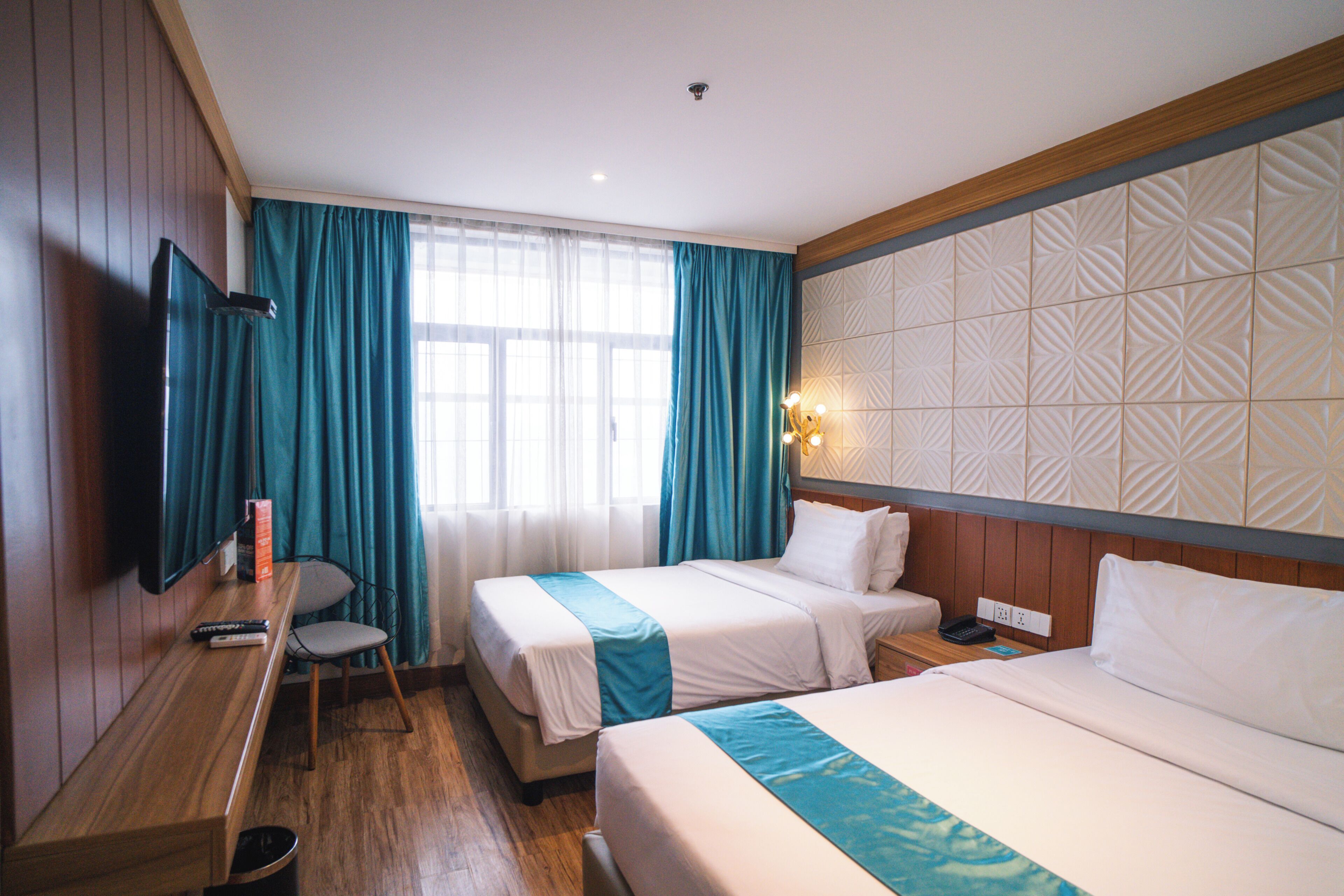 A hotel room with two beds, a desk, a chair, a TV, and a window with curtains.