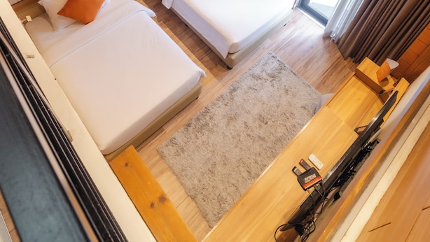 A hotel room with two beds, wooden walls, a large window, and a ceiling fan.