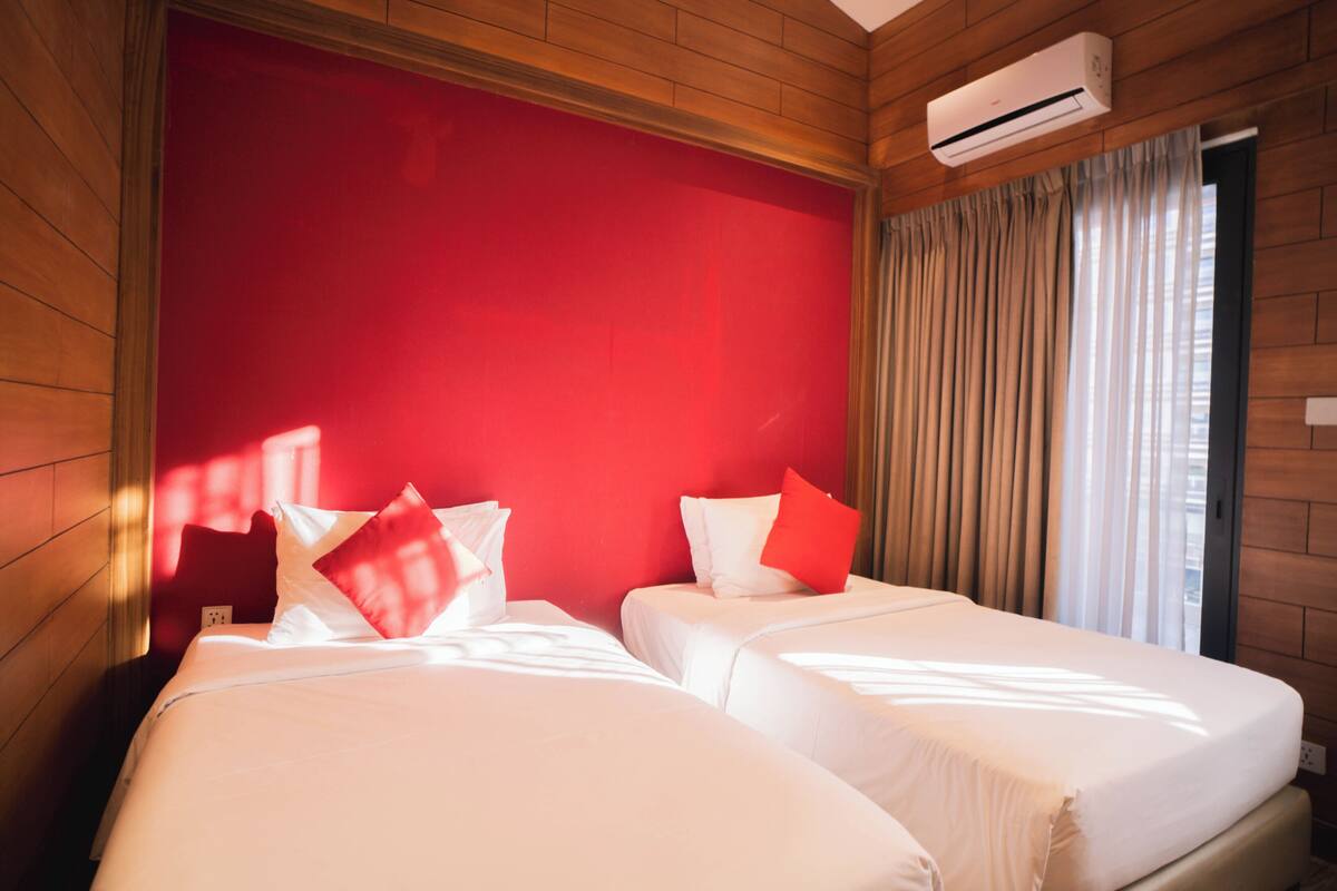 Une chambre d’hôtel avec deux lits, un mur d’accent rouge et un appareil de climatisation.
