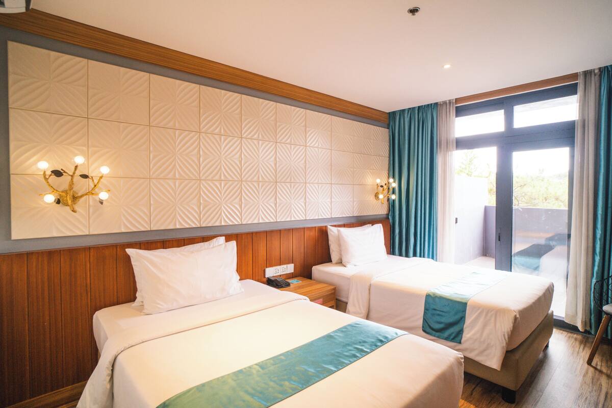 Une chambre d’hôtel avec deux lits, une tête de lit en bois, un mur à motifs et une vue sur l’extérieur, visible à travers une porte vitrée.