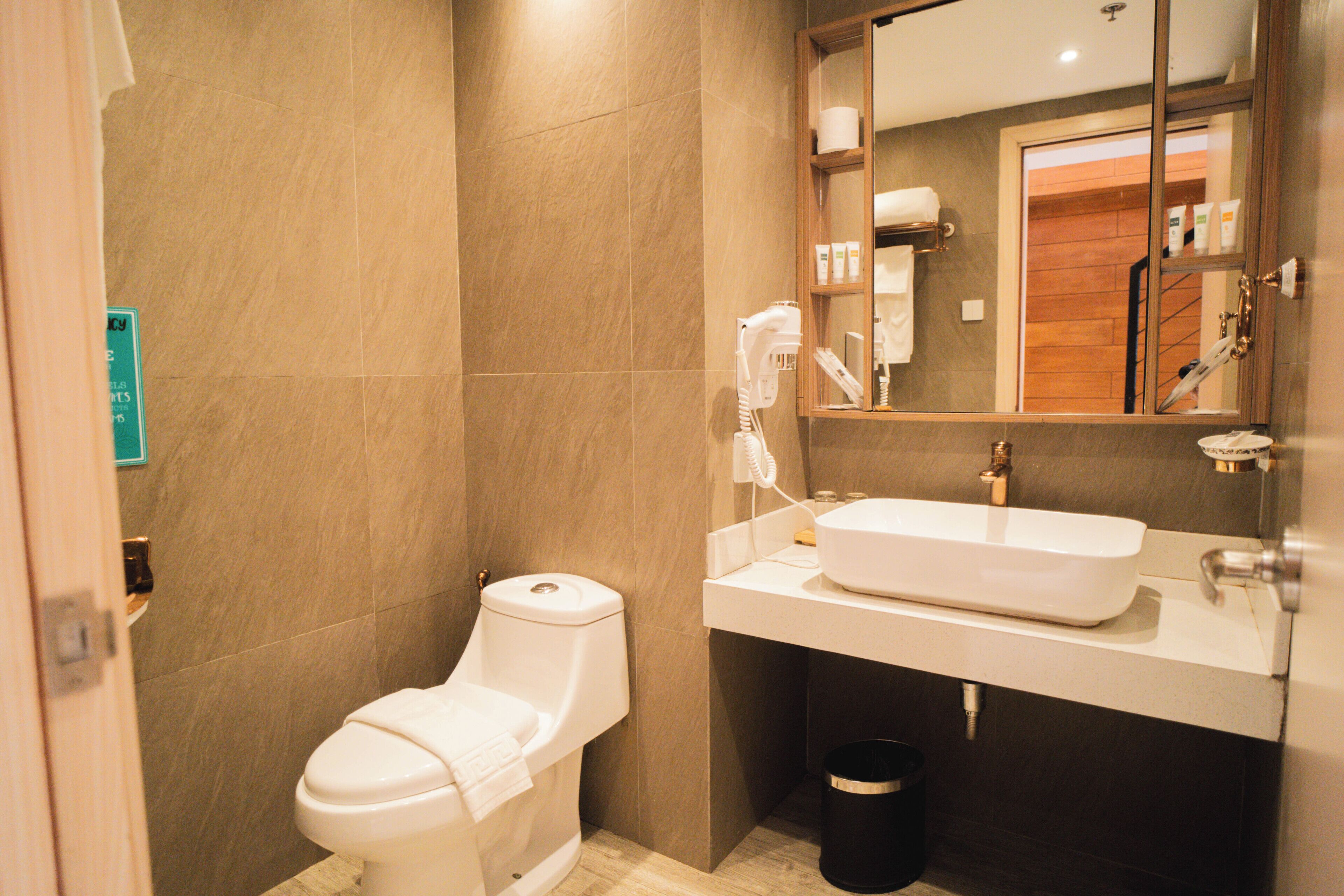 A bathroom with a toilet, sink, mirror, and a trash bin.