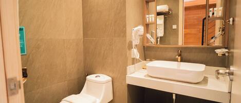 A bathroom with a toilet, sink, mirror, and a trash bin.