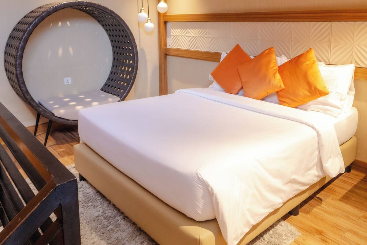 Une chambre à coucher avec un lit, un fauteuil rond en osier et une tête de lit en bois.