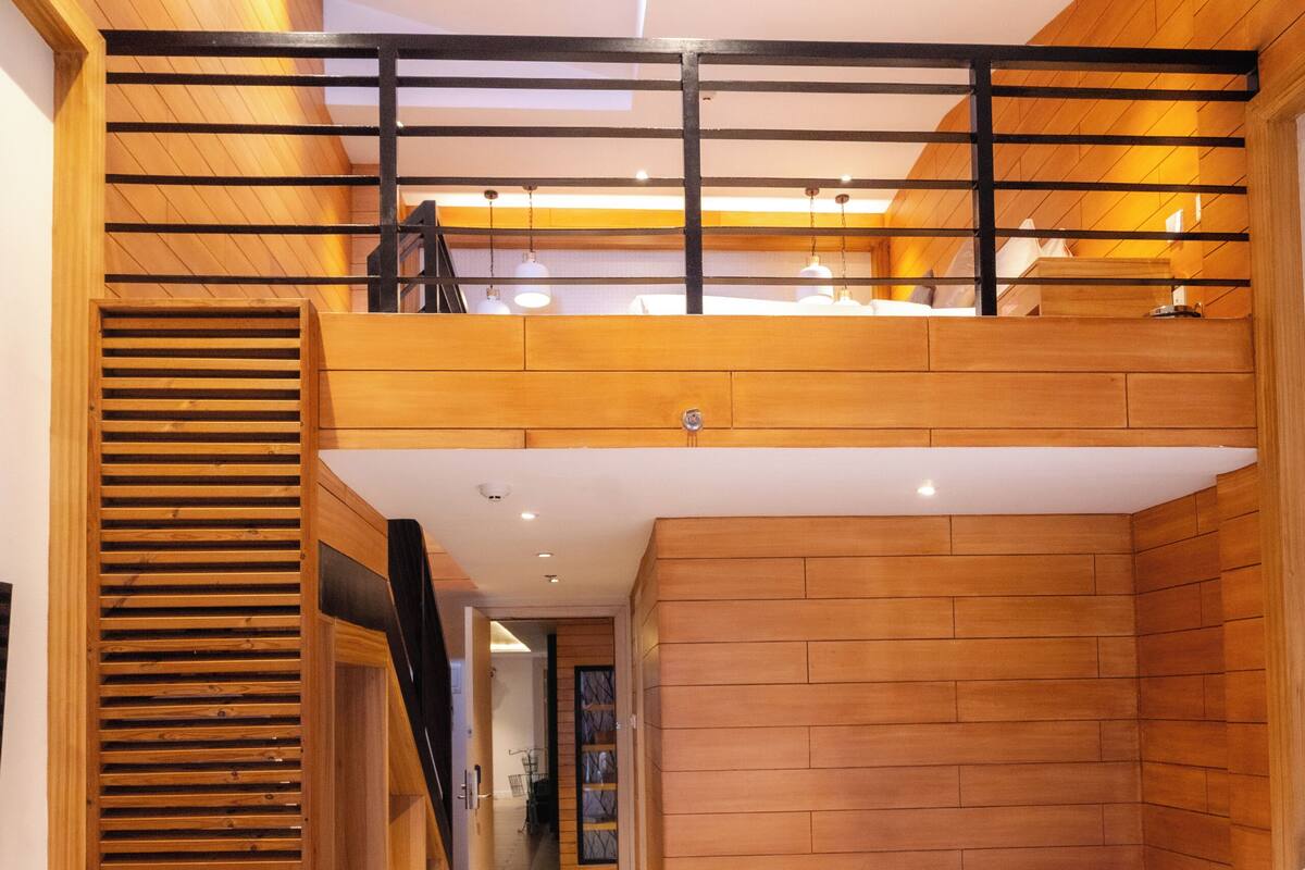 Une chambre moderne avec un espace en mezzanine, des murs en bois, un lit blanc et un bureau.